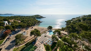 An aerial view of a coastal resort with a swimming pool, beach, and lush greenery. - Aluasoul Hotel Carolina (Capdepera)
