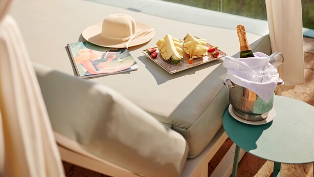 A balcony with a view of the sea, a cushioned seating area, a table with a bottle of champagne, and a plate of food. - Aluasoul Hotel Carolina (Capdepera)