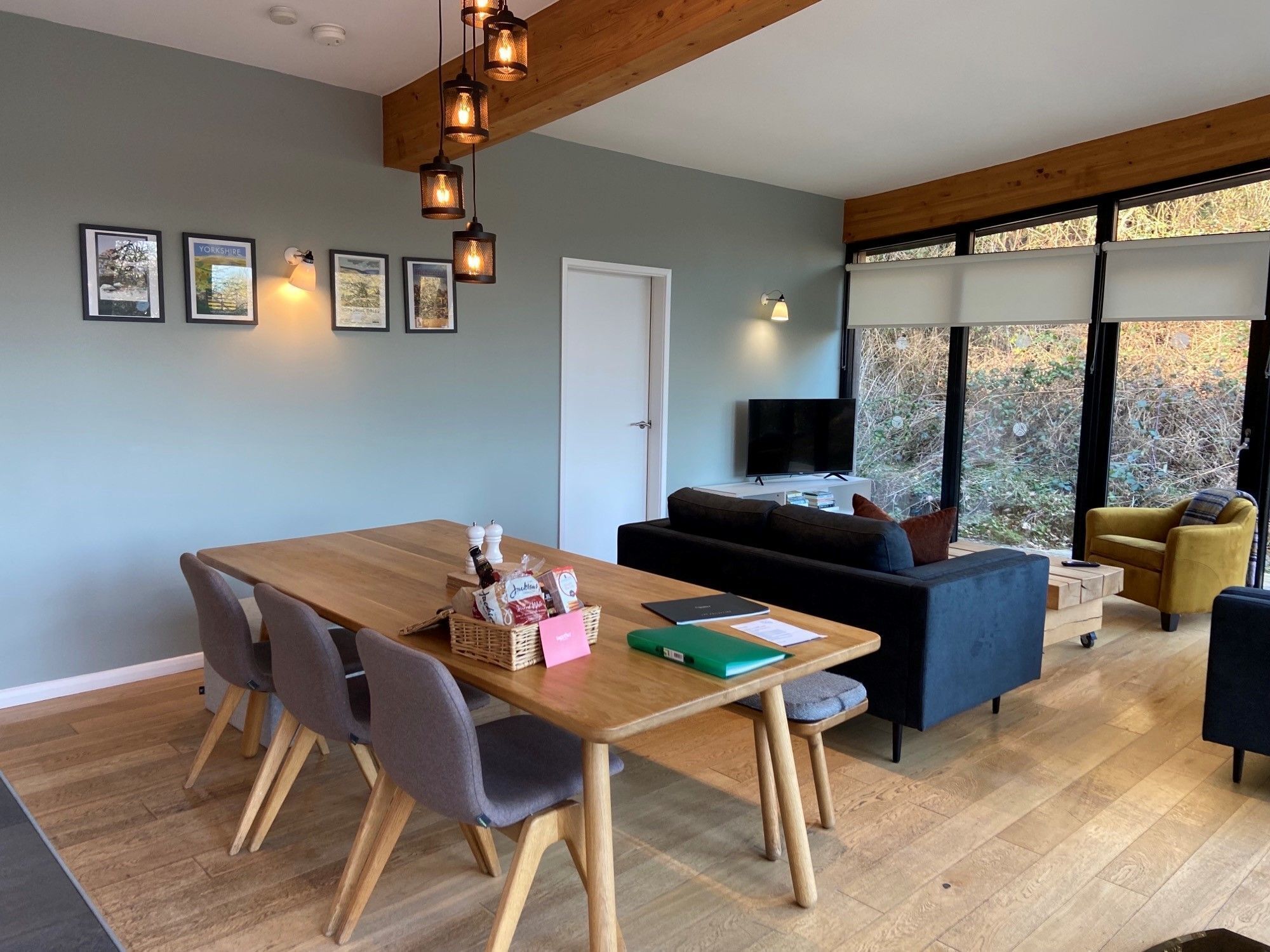 Un salon moderne avec une table à manger en bois, des chaises grises, un canapé et un téléviseur.