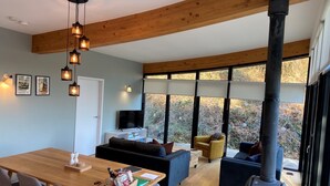 A modern living room with a wooden dining table, sofas, and a large window offering a view of the outdoors. - A yorkshire dale that sleeps 6 guests  in 3 bedrooms (Richmond)