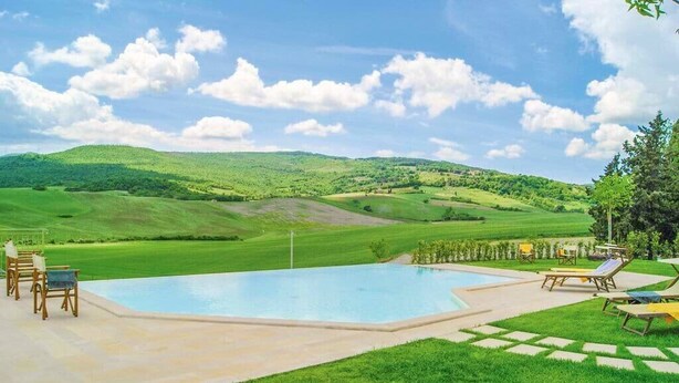 Ein Swimmingpool mit Liegestühlen und einem Tisch, umgeben von einer gepflegten Rasenfläche und Hügeln im Hintergrund.