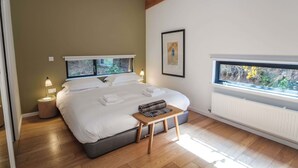Une chambre moderne avec un grand lit, des lampes de chevet, une petite table et une fenêtre donnant sur un paysage verdoyant.