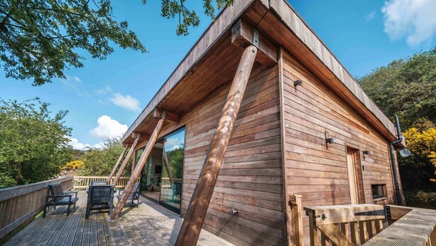 Une cabane en bois dotée d’une terrasse, de grandes fenêtres et d’une balustrade en bois.