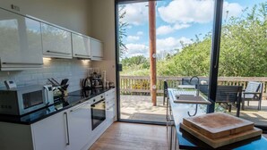 Une cuisine moderne avec des meubles blancs, un plan de travail noir et une terrasse en bois dotée d’un espace salon extérieur.