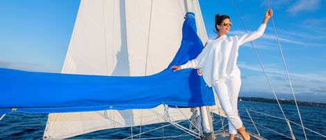 A person on a sailboat with a blue sail and white sail cover.