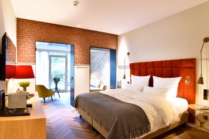 A modern hotel room with a brick wall, a large bed with white linens, a desk with a computer, and a chair.