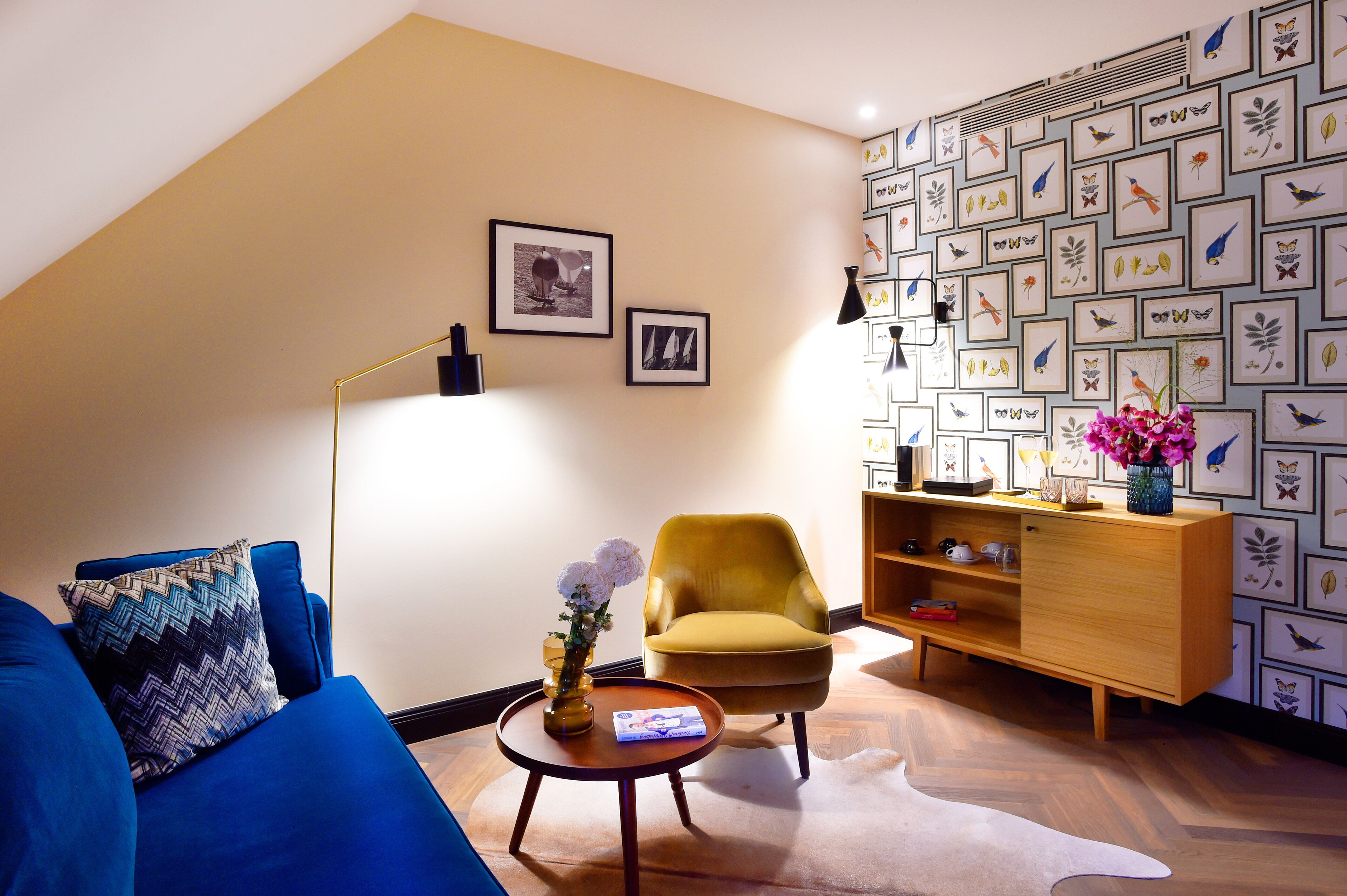 A living room with a blue sofa, a yellow armchair, a wooden cabinet, and a wall with framed bird illustrations.