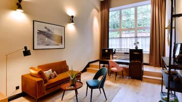 Ein modernes Wohnzimmer mit einer Couch, einem Sessel, einem Couchtisch und einem Schreibtisch mit einem Computer. Es gibt ein Fenster mit Vorhängen und ein gerahmtes Bild an der Wand.