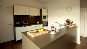 Eine moderne Küche mit weißen Schränken, einer Holz Arbeitsplatte, einer Mikrowelle, einem Backofen, einer Kaffeemaschine und einer Wanduhr.