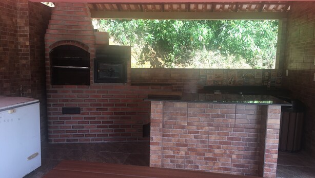 An outdoor kitchen with a brick oven, a small refrigerator, and a window overlooking greenery.