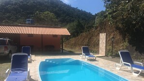 A rectangular swimming pool with blue water, surrounded by lounge chairs and a tiled patio.