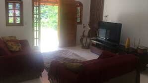 A living room with a TV, two sofas, a small table, and a wooden door leading outside.