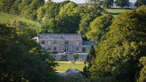 A large, two-story stone house surrounded by dense trees and a well-maintained lawn.
