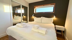 A hotel room with a large bed, a mirror, a window, and bedside lamps.