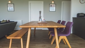 Un tavolo da pranzo in legno con panche, circondato da sedie viola, in una stanza con un divano grigio e un termosifone.
