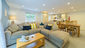 A modern living room with a sectional sofa, a dining table with chairs, and a kitchen in the background.