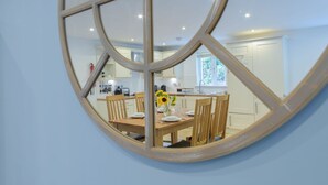 A dining area with a round mirror reflecting a kitchen and dining table set with plates, cutlery, and a vase of sunflowers.