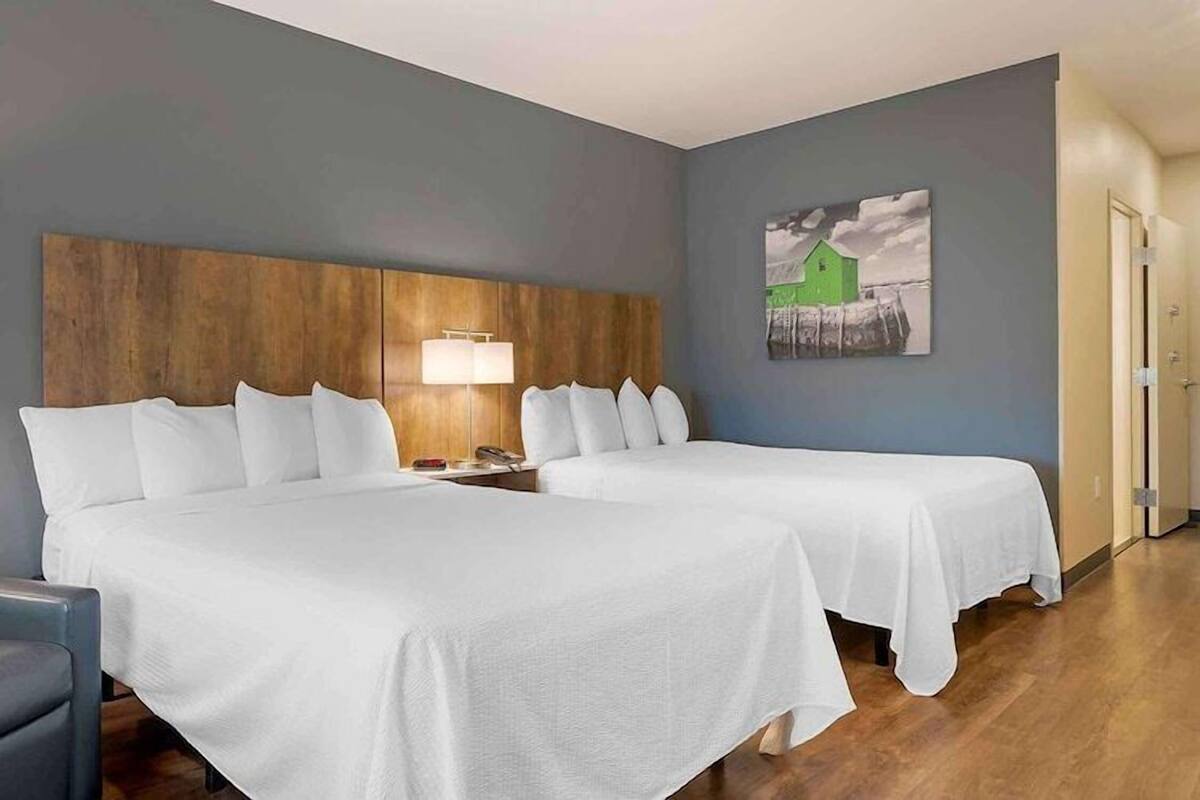 A hotel room with two beds, a desk, a chair, a lamp, and a painting on the wall.