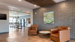 A lobby with leather armchairs, a round table, and a large mural on the brick wall. - Extended Stay America Premier Suites Savannah Pooler (Pooler)