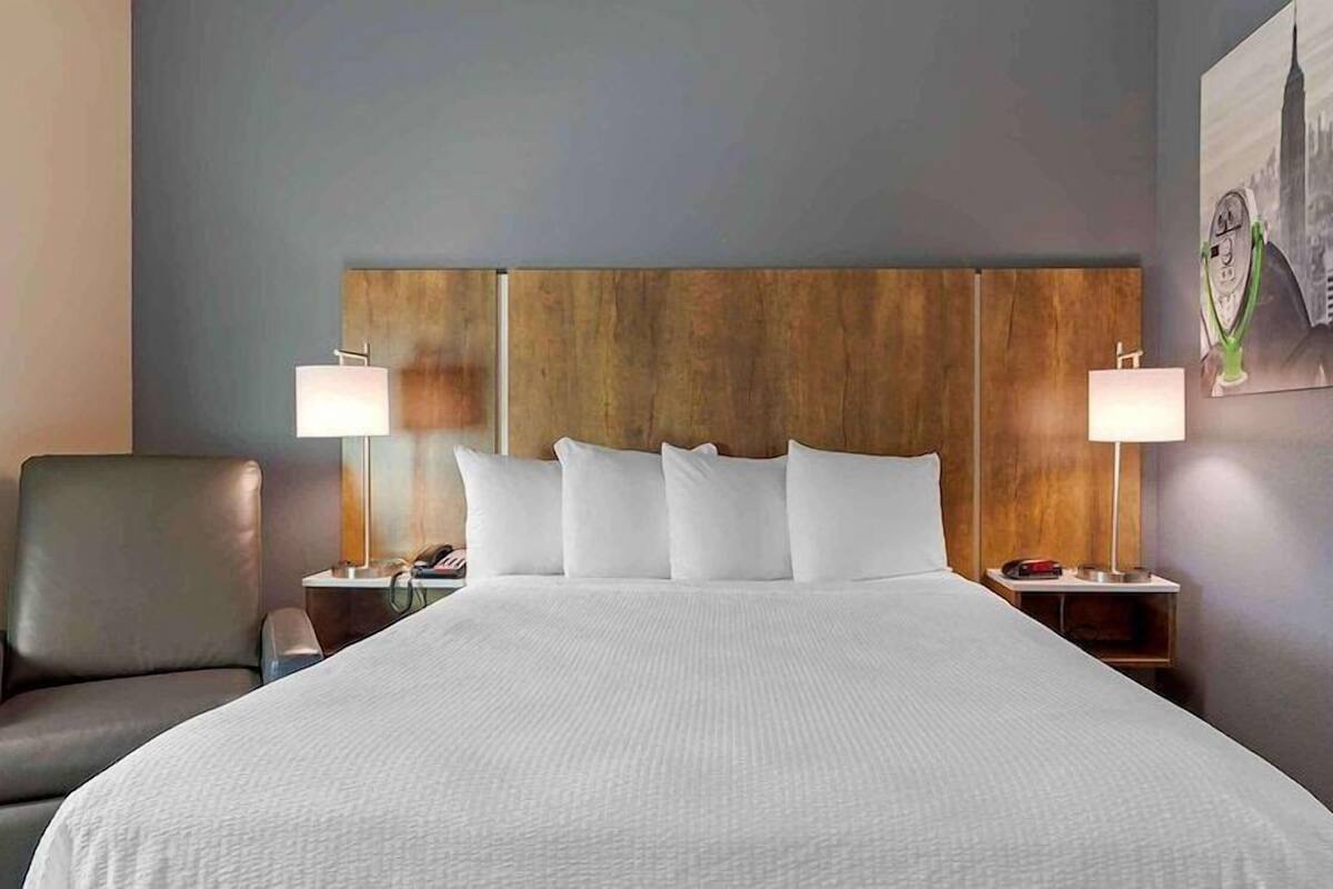 A hotel room with a large bed, two bedside tables, a chair, and a cityscape painting on the wall.