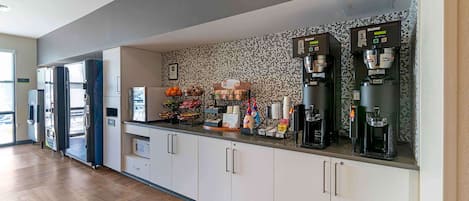 A kitchen area with a coffee machine, refrigerator, microwave, and various food items.