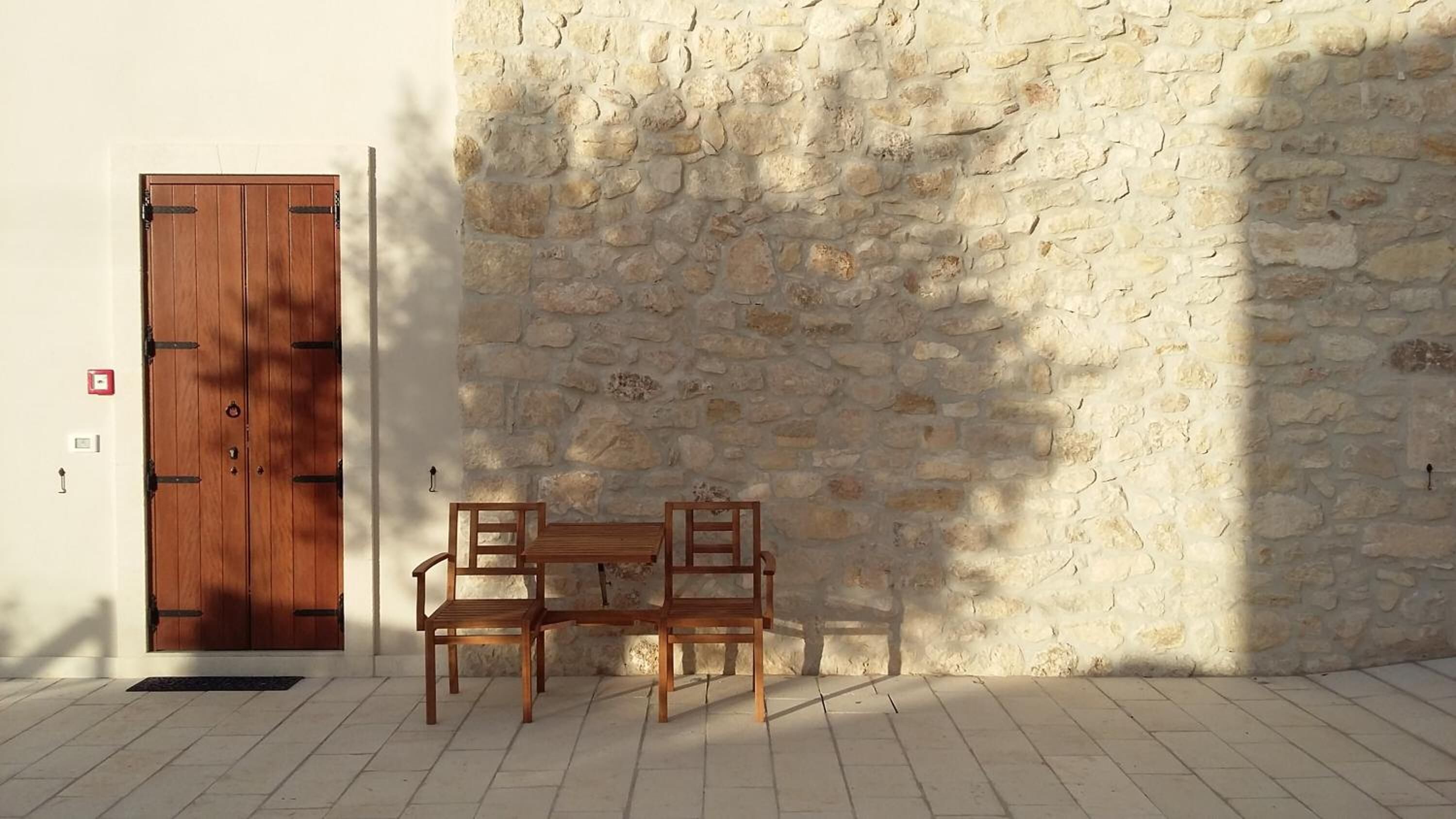 Una porta de fusta amb una paret de pedra i una taula petita amb cadires al davant.