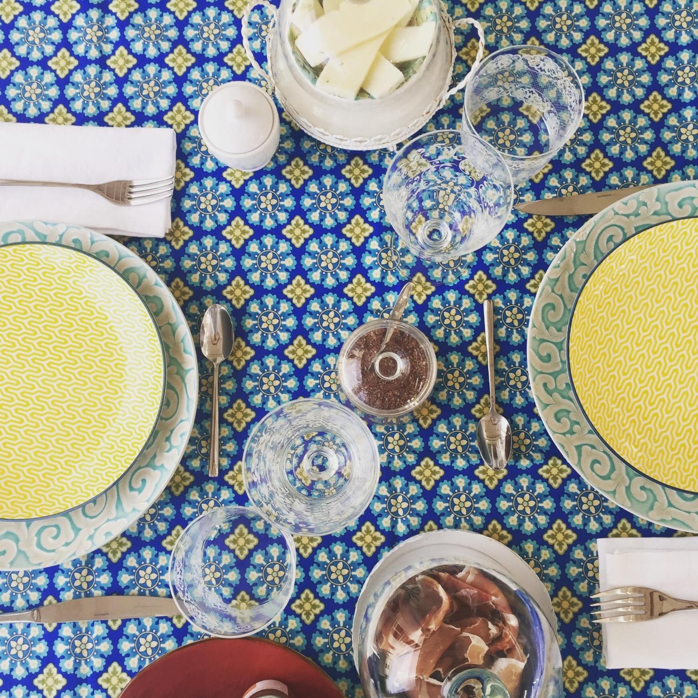 A table set with plates, bowls, glasses, and cutlery on a patterned tablecloth.