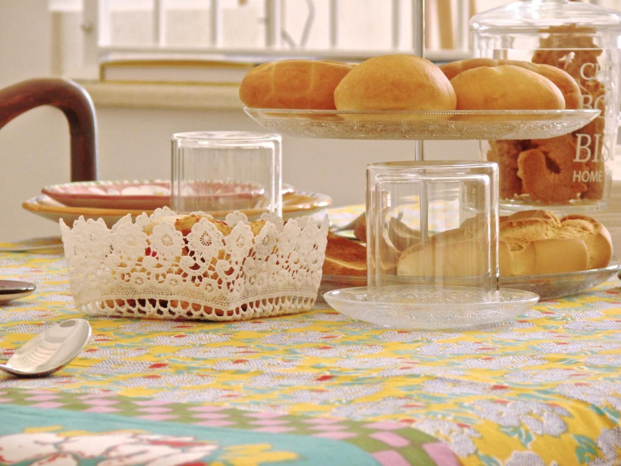 A table with a floral tablecloth, a lace basket, and a glass display case with pastries.