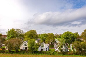 En rad traditionella hus med en grön äng i förgrunden och en molnig himmel ovanför.