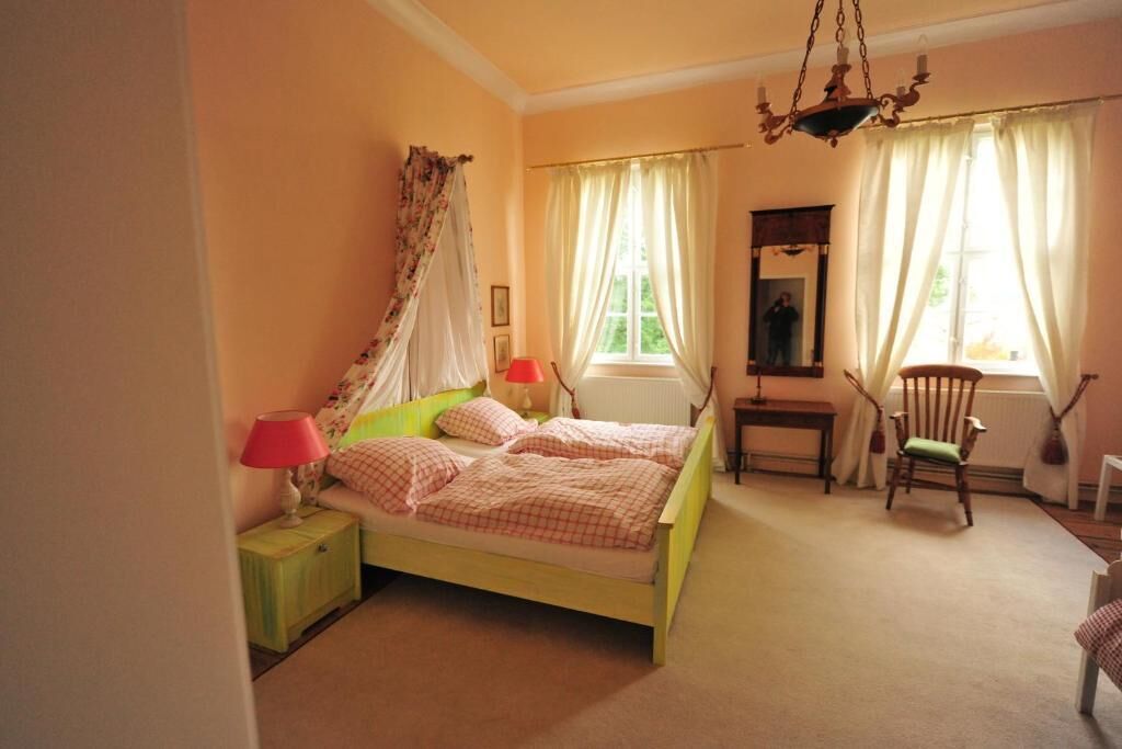 A bedroom with a bed, bedside tables, a chair, a mirror, and a window with curtains.