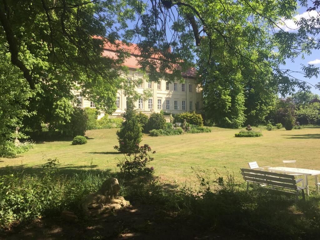 A large, classical building with a red roof, surrounded by a well-maintained lawn and trees.