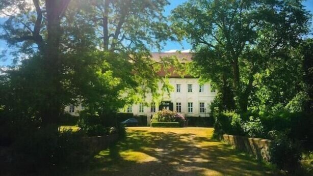 Un edificio bianco con facciata simmetrica, immerso nel verde e sotto un cielo sereno.
