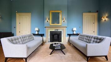 A room with two grey sofas, a black coffee table, a fireplace, and two doors with wall sconces.