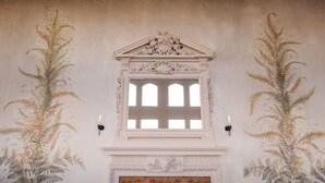 Een kamer met een open haard, een decoratieve haardmantel en een raam omlijst door sierlijke moulures.