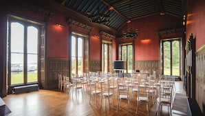 Ein großer Saal mit Sitzreihen für eine Veranstaltung, großen Fenstern und einer hohen Decke mit aufwändiger Dekoration.
