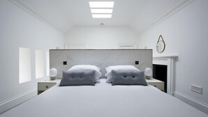Ein modernes Schlafzimmer mit einem großen Bett, zwei Nachttischen, einem Marmorkopfschild und einem Kamin.