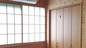 Ein Zimmer mit Holzwänden, einem Tatami-Bodenbelag, einer Schiebetür und einer Decken-Klimaanlage.