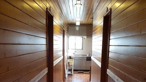 Ein schmaler Korridor mit Holzwänden und Holzdielen, der zu einem Küchenbereich mit einem Fenster führt.