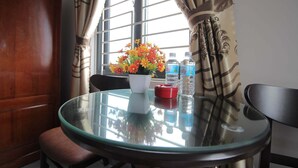 A round glass table with a white vase of flowers, two water bottles, and a red object on a wooden floor. - Phu Xuan Hotel (Quy Nhon Nam)