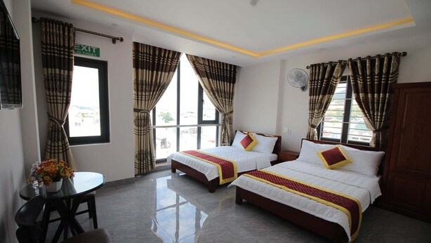 A hotel room with two beds, a small table with a vase of flowers, and a chair. - Phu Xuan Hotel (Quy Nhon Nam)