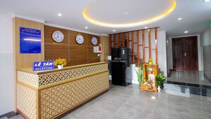 A reception desk with a clock, a sign for the reception, and a decorative plant. - Phu Xuan Hotel (Quy Nhon Nam)