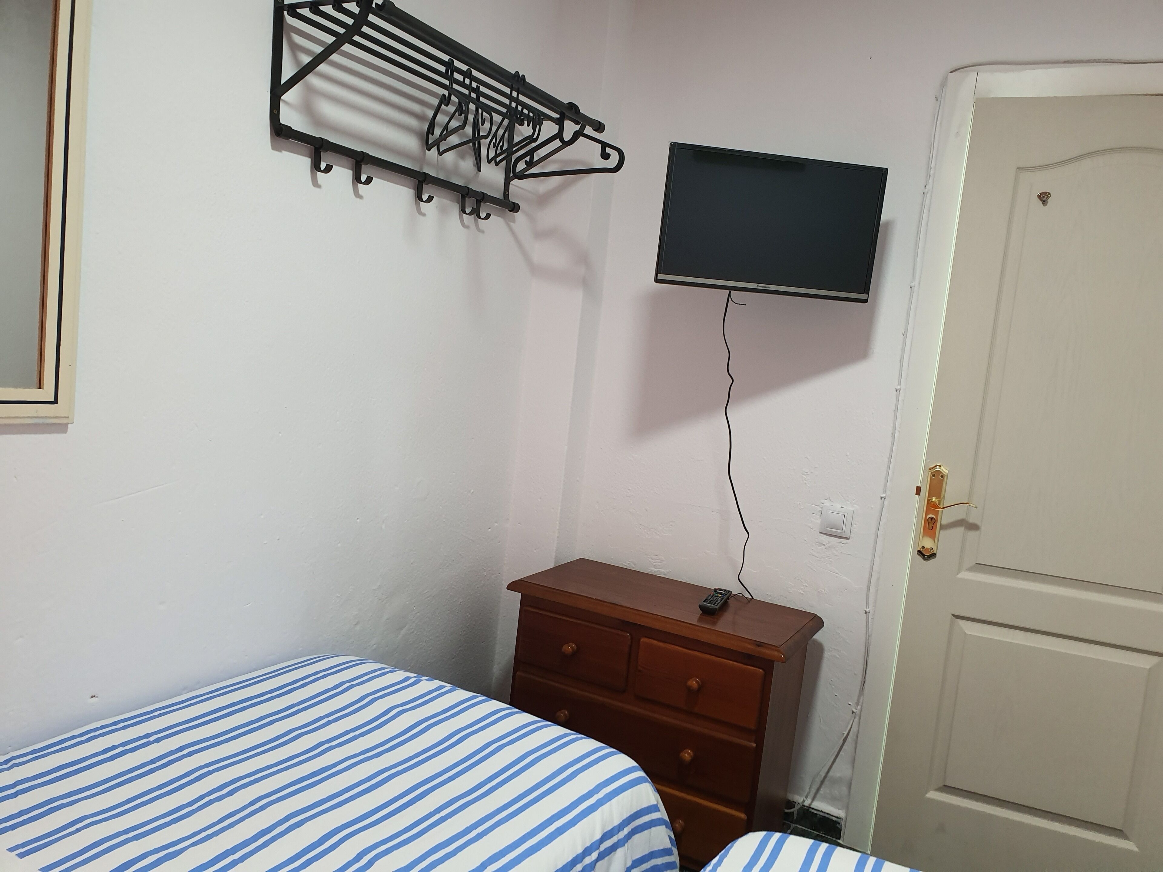 A bedroom with a bed, a wooden dresser, a TV mounted on the wall, and a door.