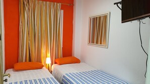 A room with two beds, orange curtains, a single lamp, and a TV mounted on the wall.