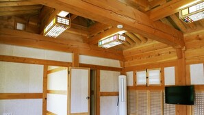 A spacious room with wooden beams, a large sliding door, a standing heater, a television mounted on the wall, and a window with a stained glass design. - Hadong Today Sun Hanok Traditional House (Hadong)