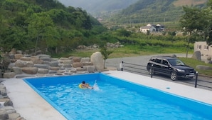 A swimming pool with a person in the water, surrounded by rocks and a parked car. - Hadong Today Sun Hanok Traditional House (Hadong)