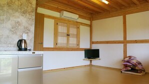 A room with a wooden ceiling, a television on a stand, a tiled wall, and a small cabinet with a kettle. - Hadong Today Sun Hanok Traditional House (Hadong)