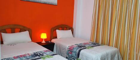 Une chambre d’hôtel avec deux lits, une table de chevet avec une lampe, un tableau au mur et un rideau à rayures.