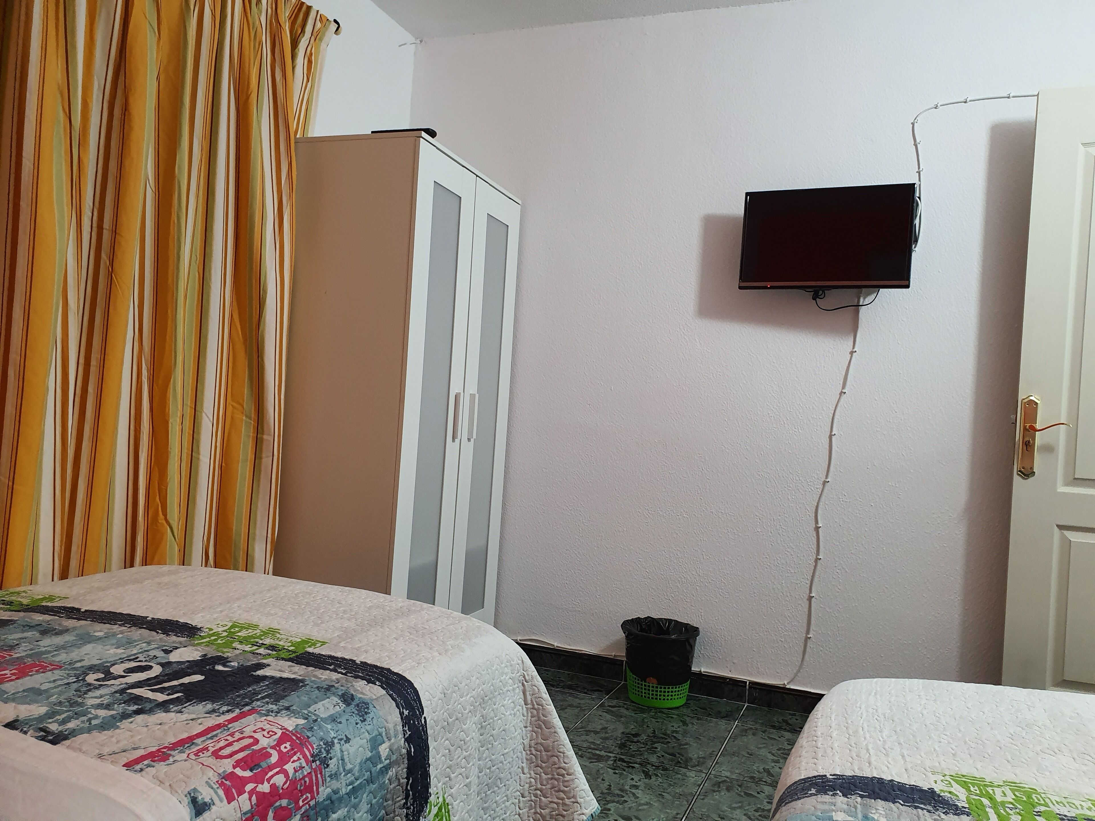 A hotel room with two beds, a wardrobe, a TV mounted on the wall, and a trash bin.