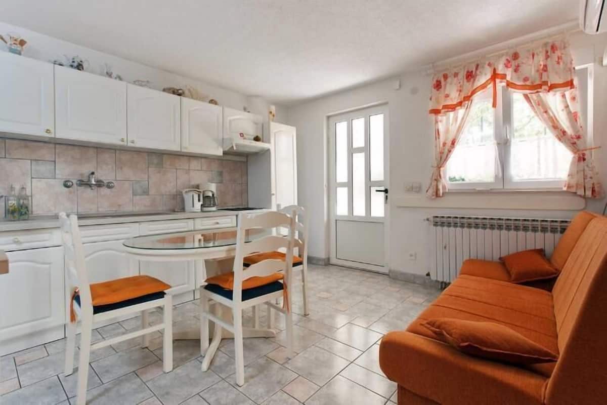 Eine kleine Küche mit weißen Schränken, ein Esstisch mit zwei Stühlen und ein Sofa im Wohnbereich.