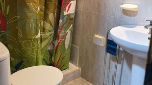 A bathroom with a toilet, a shower with a floral curtain, a sink with a mirror, and tiled walls. - Low Cost Room Plaza de Hierro II (San Bartolomé de Tirajana)